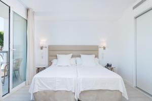 a white bedroom with a large bed and a balcony at Aparthotel Ses Fotges in Playa de Muro