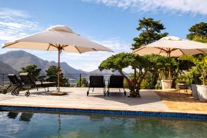 a swimming pool with two umbrellas and chairs next to a swimming pool at Dreamhouse Guest House in Hout Bay