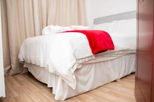 a white bed with a red blanket on it at Crystal Apartments in Lilongwe