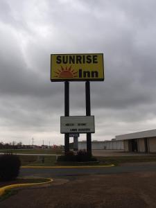 ein Schild für ein Gasthaus am Straßenrand mit Sonnenuntergang in der Unterkunft Sunrise Inn Lake Charles in Lake Charles