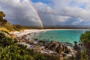 un arco iris sobre una playa con rocas y el océano en THE TIN SHED Couples accommodation at Bay of Fires en Binalong Bay