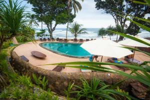 a swimming pool with an umbrella and the ocean at Pondok Pitaya Balian Hotel in Selemadeg