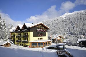 a large yellow building with snow on the ground at Hotel Cime D'Oro in Madonna di Campiglio