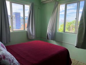 Un dormitorio con dos ventanas y una cama con una manta roja. en Residencial De Aluguel, en Bombinhas