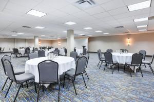 Holiday Inn Express Winnipeg Airport - Polo Park, an IHG Hotel في وينيبيغ: قاعة احتفالات بالطاولات البيضاء والكراسي