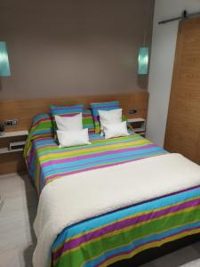 a large bed with colorful striped sheets and pillows at The Little House Sir in Ávila