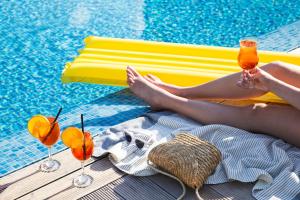 una donna seduta accanto alla piscina con bevande di Leonardo City Tower Hotel Tel Aviv a Tel Aviv