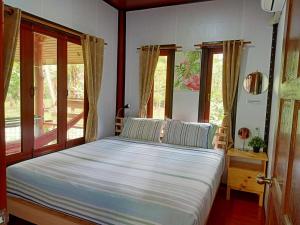 a bedroom with a large bed with white sheets and windows at Baan Moonchan House in Chaloklum