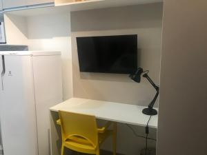 a desk with a television on a wall with a lamp and yellow chairs at Suites Metrô Luz in Sao Paulo