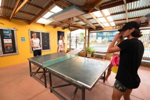 um grupo de pessoas em pé em torno de uma mesa de pingue-pongue em Ozzie Pozzie Backpackers - Port Macquarie YHA em Port Macquarie