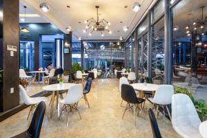 a restaurant with white tables and chairs and windows at Bamboo Hotel in Da Nang