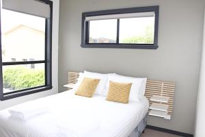 a bedroom with a white bed with two windows at Cove View Retreat in St Helens