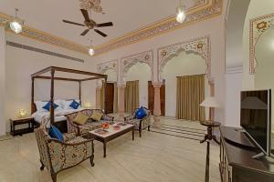 a room with a bed and a couch and a tv at The Jai Bagh Palace in Jaipur