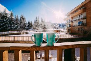 two coffee mugs sitting on a wooden railing with the snow at BAKURIANI PLAZA A-208 in Bakuriani