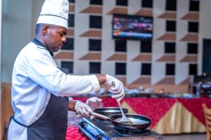 a man cooking food in a pan on a stove at Kigaliview Hotel and Apartments in Kigali