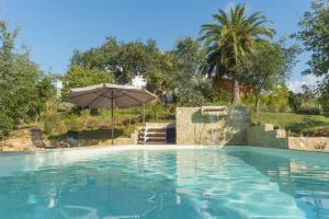 a swimming pool with an umbrella and some trees at Herdade Quinta Natura Turismo Rural in Aljezur
