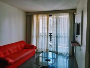 un soggiorno con divano rosso e tavolo in vetro di Hotel Flat Atlântico, Apartamento Com 02 Quartos a Fortaleza