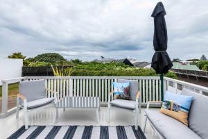 - une terrasse avec 2 chaises, une table et un parasol dans l'établissement Awesome Beach House on Oceanview Road, à Mount Maunganui