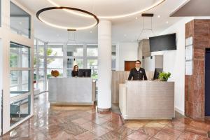 two people standing at the reception desk in a lobby at H+ Hotel Limes Thermen Aalen in Aalen