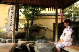 una mujer en un kimono sentada junto a una fuente en Ougiya Ryokan, en Toyooka