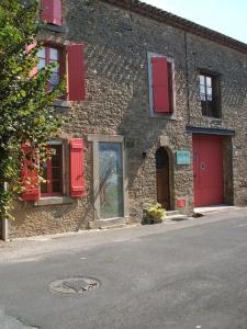 a stone building with red shuttered windows and a street at Chambres d'hôtes Sous L'Olivier in Trausse