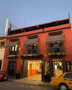 a red building with balconies and a yellow car parked in front at Hotel Jiménez in Oaxaca City