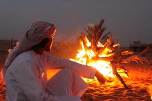 una mujer sentada junto a una hoguera en una playa en Nomadic Desert Camp, en Al Wāşil