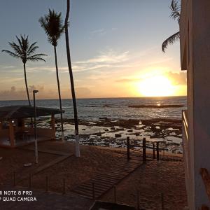 um pôr-do-sol numa praia com palmeiras e o oceano em Apartamento duplex em Arembepe em Arembepe
