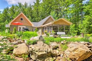 a house in the woods with rocks in the yard at Waterfront Great Pond Cottage with Hot Tub and Deck! in Aurora