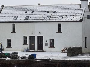 a white building with snow on the ground in front of it at 2 The Noust Self Catering in Saint Margarets Hope