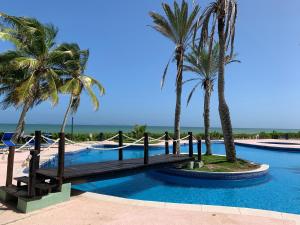 a swimming pool with palm trees and a wooden bridge at Cimarron Suites Playa Parguito in Aricagua