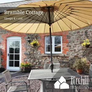 einem Tisch mit einem Regenschirm vor einem Gebäude in der Unterkunft Birchill Farm & Cottages - Bramble Cottage in Great Torrington