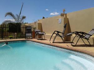 een zwembad met twee stoelen naast een huis bij Come Home in Oudtshoorn Self-Catering Units in Oudtshoorn