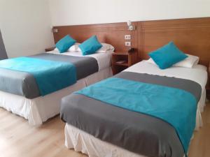 two beds in a hotel room with blue pillows at Hotel Real in Linares