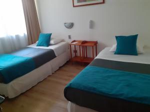Habitación con 2 camas con almohadas azules y mesa. en Hotel Real en Linares
