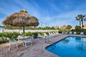 a pool with chairs and a straw umbrella and a table and chairs at Walk to Madeira Beach Coastal Condo with Balcony in St Pete Beach