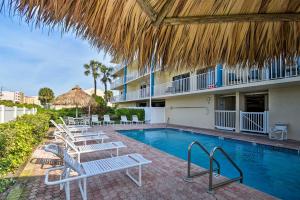 a swimming pool with chairs and a straw umbrella at Walk to Madeira Beach Coastal Condo with Balcony in St Pete Beach