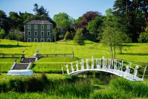 un puente blanco sobre un estanque frente a una casa en Ardnavaha House - Poolside Cottages, en Clonakilty