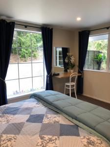 a bedroom with a bed and a desk and windows at Kānuka Cottage - Tranquil and relaxing in Akaroa