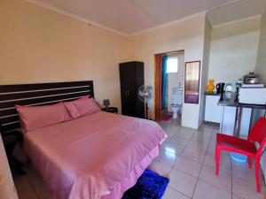 um quarto com uma cama rosa e uma cadeira vermelha em Hillside View Guesthouse em Coffee Bay