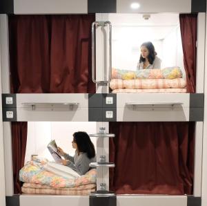 two women sitting on bunk beds reading a book at 大田市ゲストハウス 雪見院 Guesthouse Yukimi-inn in Ōda