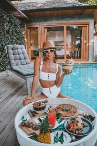 a woman sitting at a table with food next to a pool at Tango Luxe Beach Villa, Koh Samui in Choeng Mon Beach +156 photos