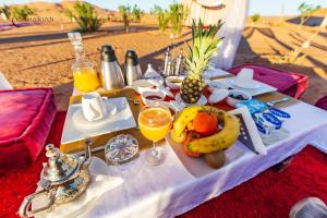 a table with a plate of fruit and drinks on it at Sahara Merzouga Luxury Camp in Merzouga