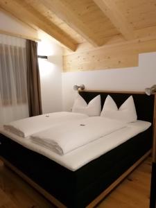 uma cama com lençóis brancos e almofadas num quarto em Studler Hofchalets em Oberperfuss