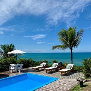 a pool with chairs and a palm tree and the ocean at Pousada Jakuara in Arraial d'Ajuda