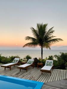 a deck with lounge chairs and a palm tree and the ocean at Pousada Jakuara in Arraial d'Ajuda