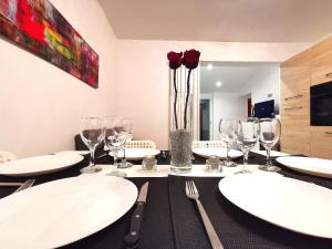 una mesa con platos blancos, copas de vino y rosas rojas en Suite Barthelemy - Spa et Sauna, en Melun