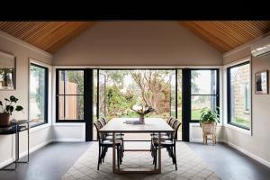 a dining room with a table and chairs and windows at Lon Retreat in Point Lonsdale