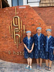 Nine Hotel Chiangmai في شيانغ ماي: ثلاث نساء بالزي الأزرق يقفن أمام جدار من الطوب