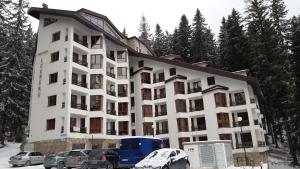 un gran edificio blanco con coches aparcados en la nieve en Апартамент Winter home Iceberg, en Pamporovo
